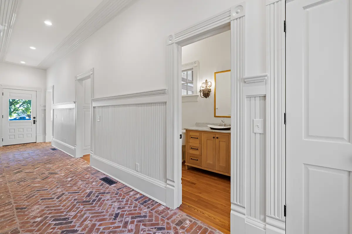 Hallway with brick flooring, wainscoting, doorways, and decorative molding