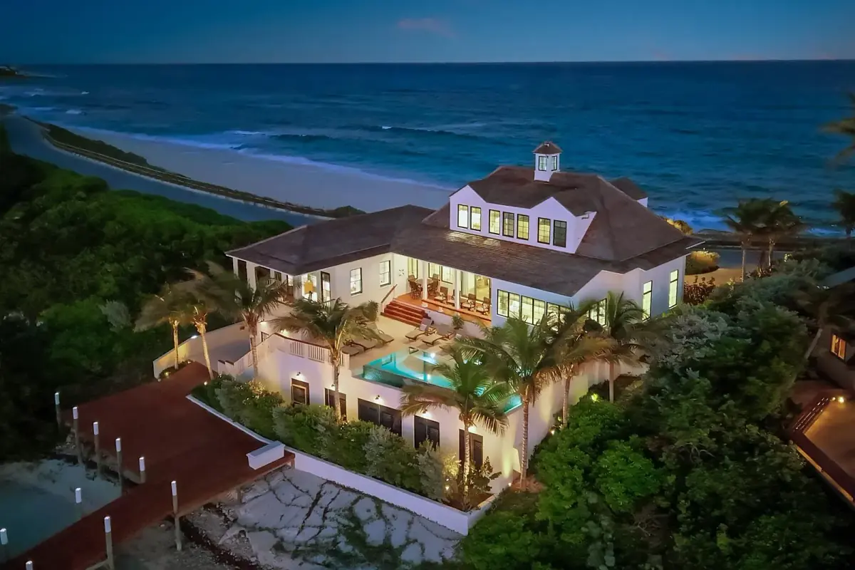 Rear exterior view of a two-story house with terrace, pool, palm trees, and beach access.