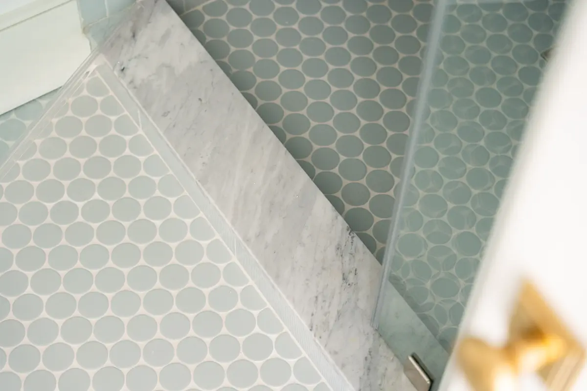 Bathroom with circular patterned tiles, marble transition, and glass shower enclosure.