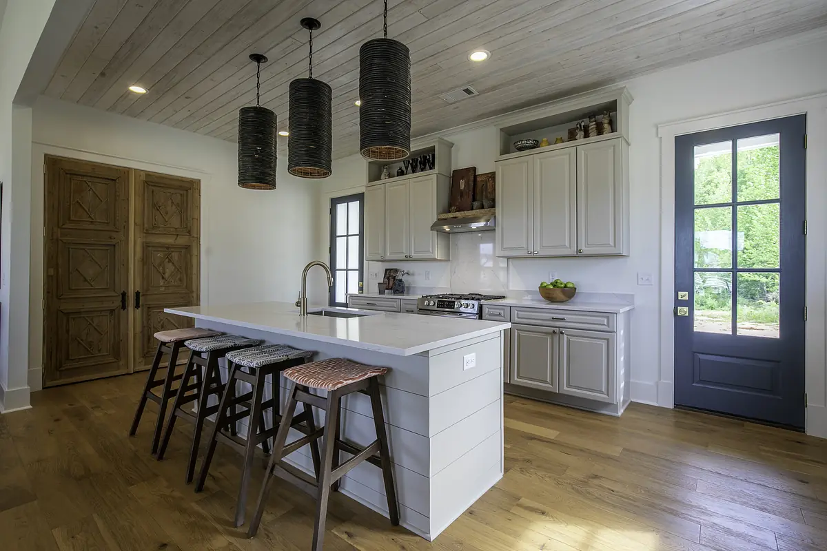 Kitchen with gray island, bar stools, wood cabinetry, stainless steel oven, and hardwood floor.