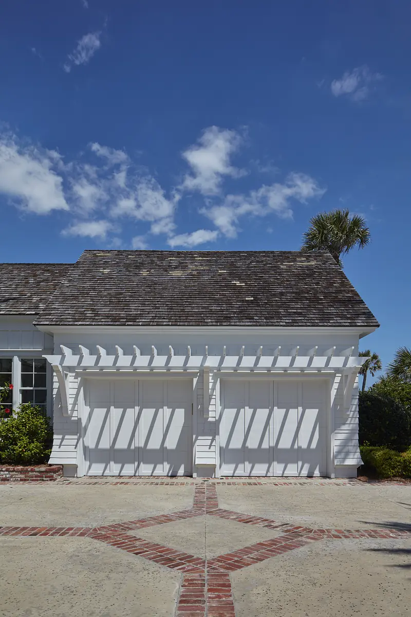 Garage with two white doors, brick path, and white siding with a trellis.