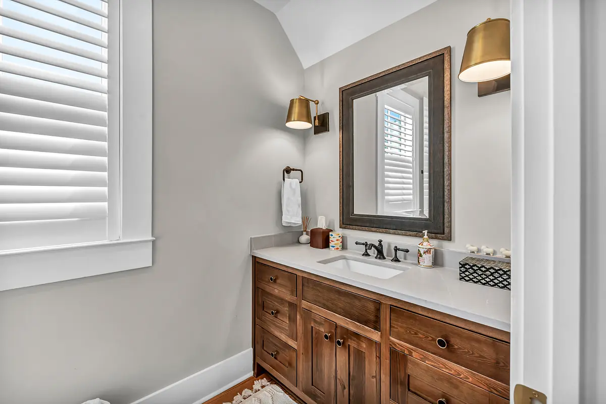 Bathroom with wooden vanity, double sinks, mirror, wall sconces, and natural light from a window.