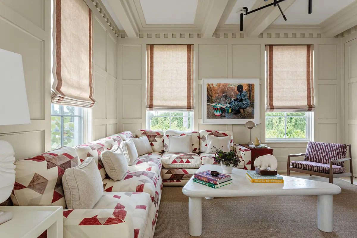Living room with sectional sofa, white table, windows with shades, and wall painting.