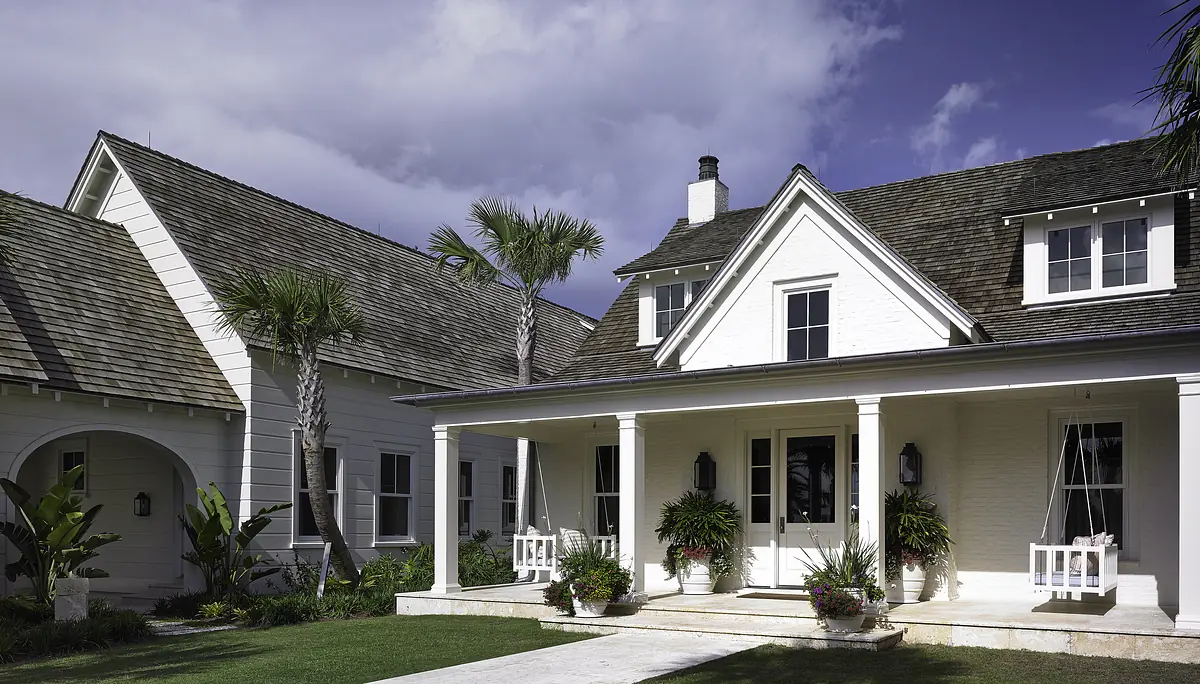 Front exterior view of a house with porch, white brick facade, palm trees, and stone path.