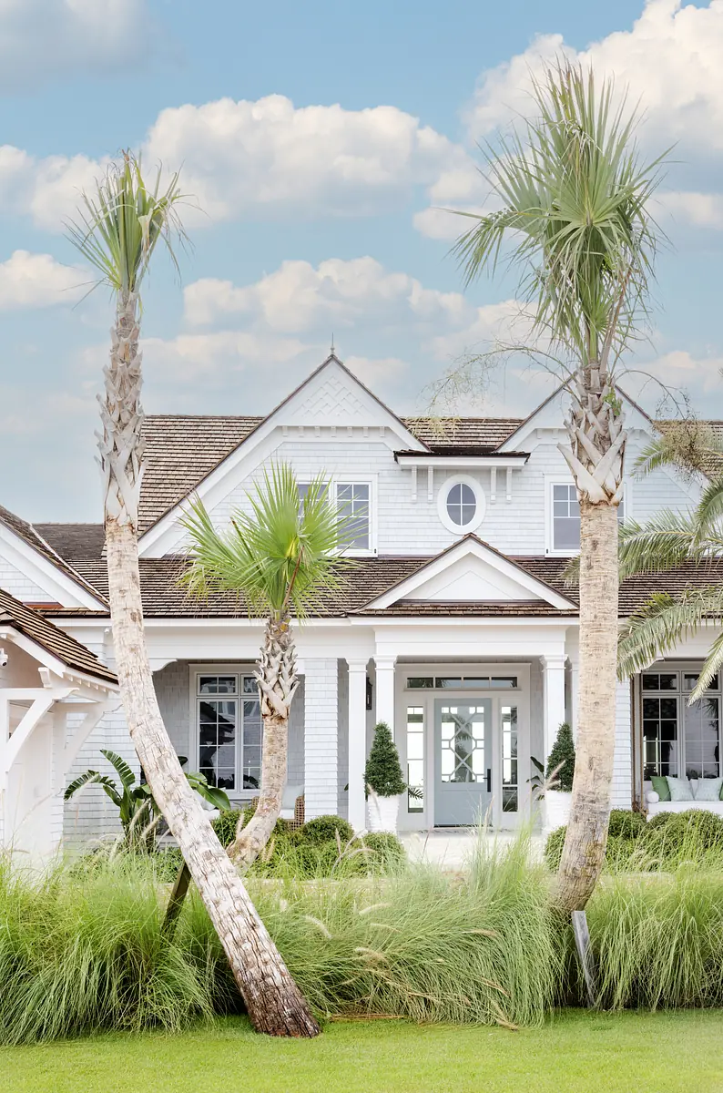 Front exterior of house with light blue facade, double door, palm trees, and grassy landscape.