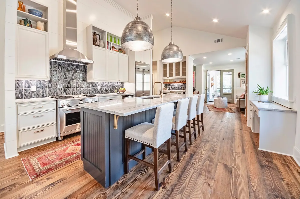 Kitchen with large island, gray cabinetry, stainless steel appliances, pendant lights, and patterned backsplash.