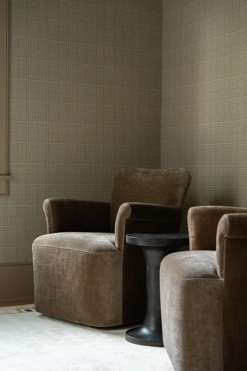 Seating area with two upholstered chairs, black side table, and plaid wallpaper.