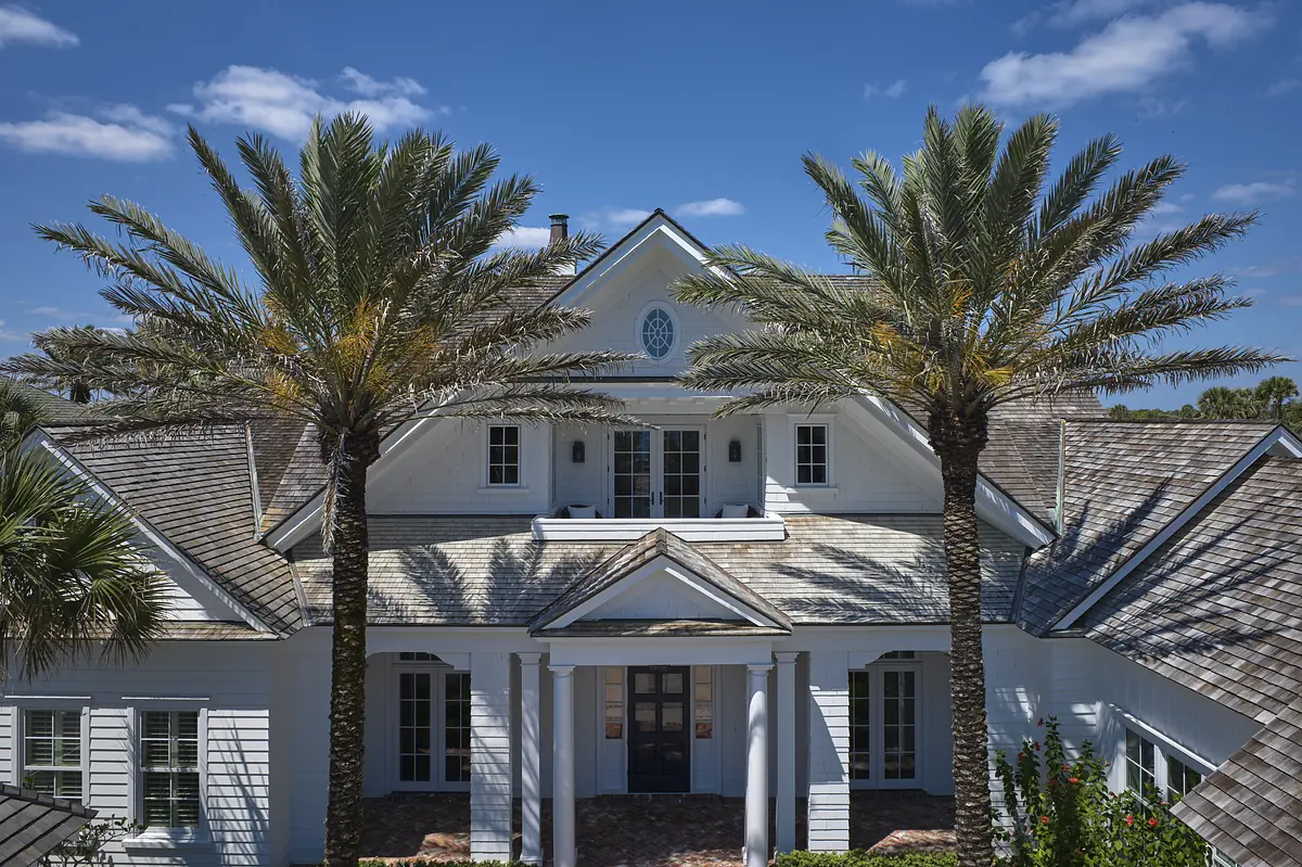 Front exterior of a house with white facade, double door entry, palm trees, and multiple gables.
