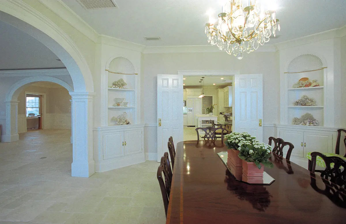 Dining room with wooden table, upholstered chairs, chandelier, built-in shelves, and archways.