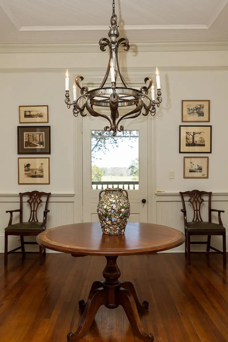 Dining room with round wood table, two chairs, decorative vase, framed artwork, and hardwood flooring