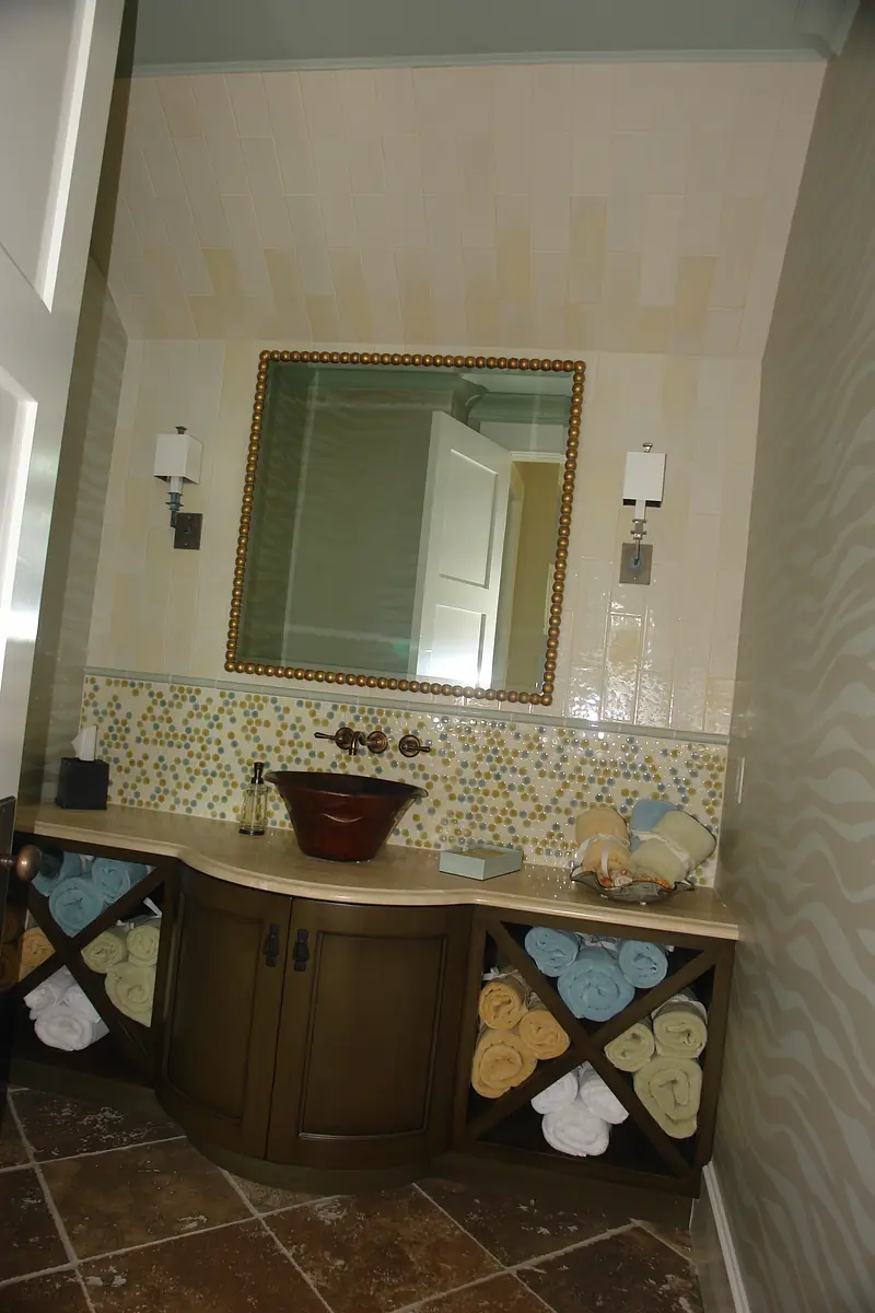 Bathroom with wooden vanity, brown vessel sink, colored tile backsplash, and rolled towels