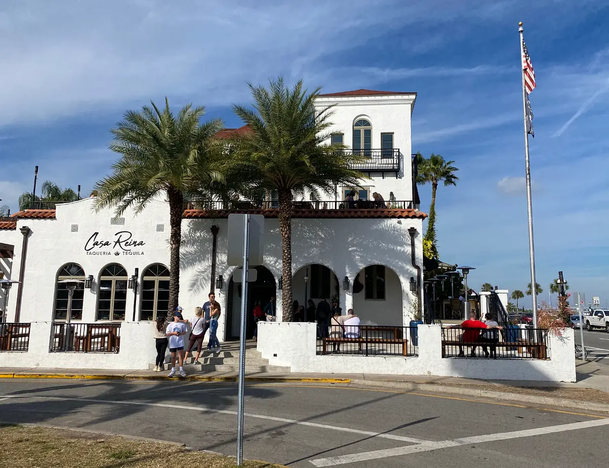 Exterior of Casa Rio with white stucco, red tile roof, palm trees, and outdoor seating.
