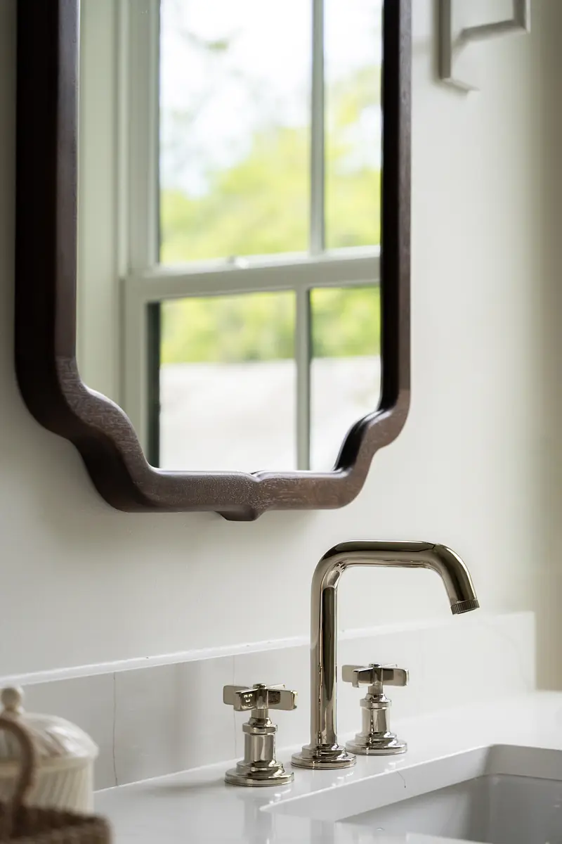 Bathroom with white countertop, sink, dark wooden mirror frame, and window for natural light.