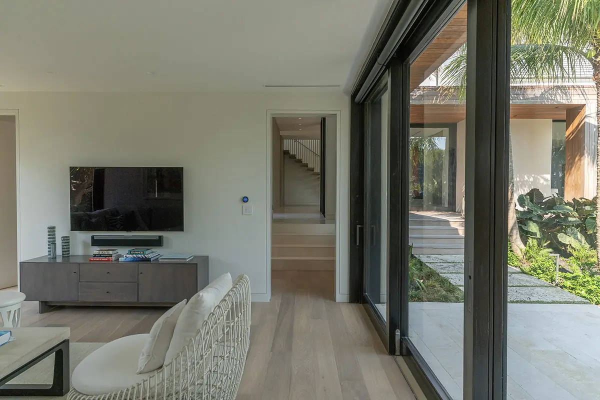 Living room with white woven chair, gray media console, large glass sliding doors, and visible staircase.