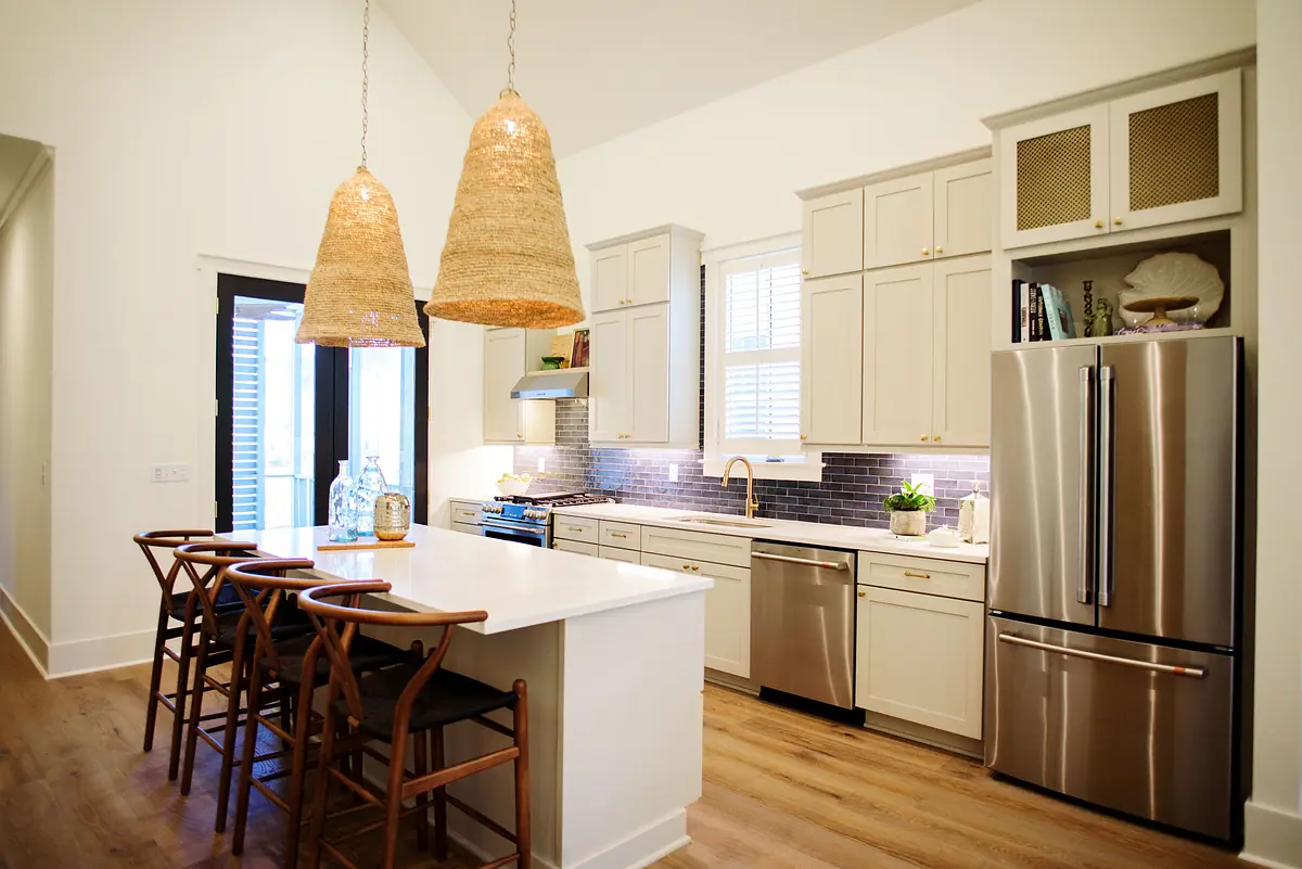 Kitchen with white island, bar stools, stainless steel appliances, beige cabinetry, and woven pendant lights.