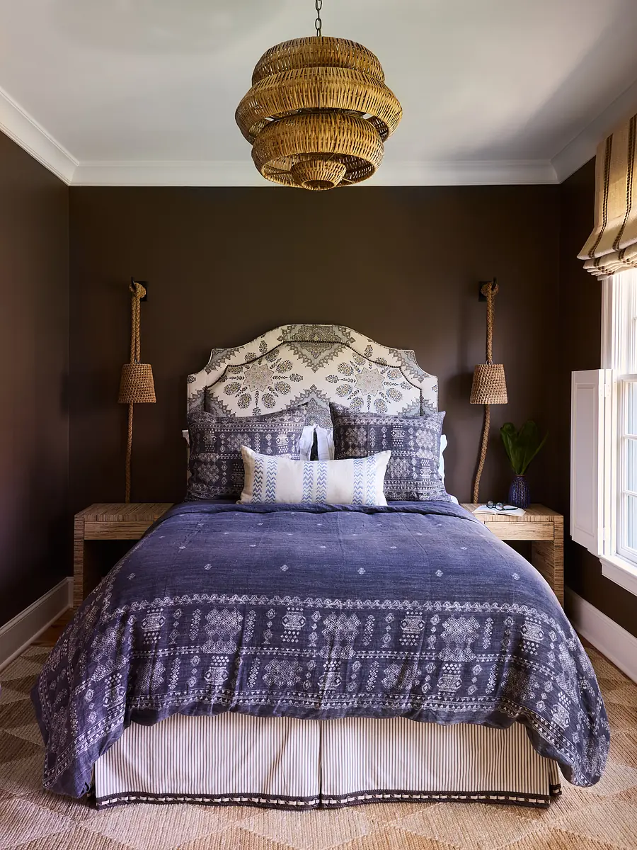 Bedroom with patterned bed, nightstands, sconces, large window, and natural fiber rug.
