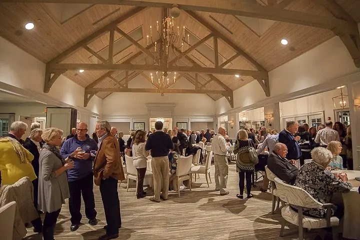 Gathering space with vaulted ceilings, wooden beams, area rug, mirrors, and chandelier with people mingling