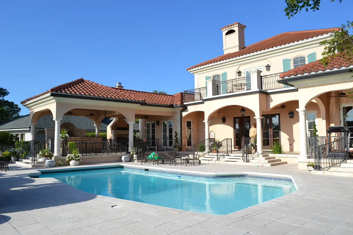 Exterior rear area with swimming pool, tiled patio, columns, and a two-story house with red-tiled roof
