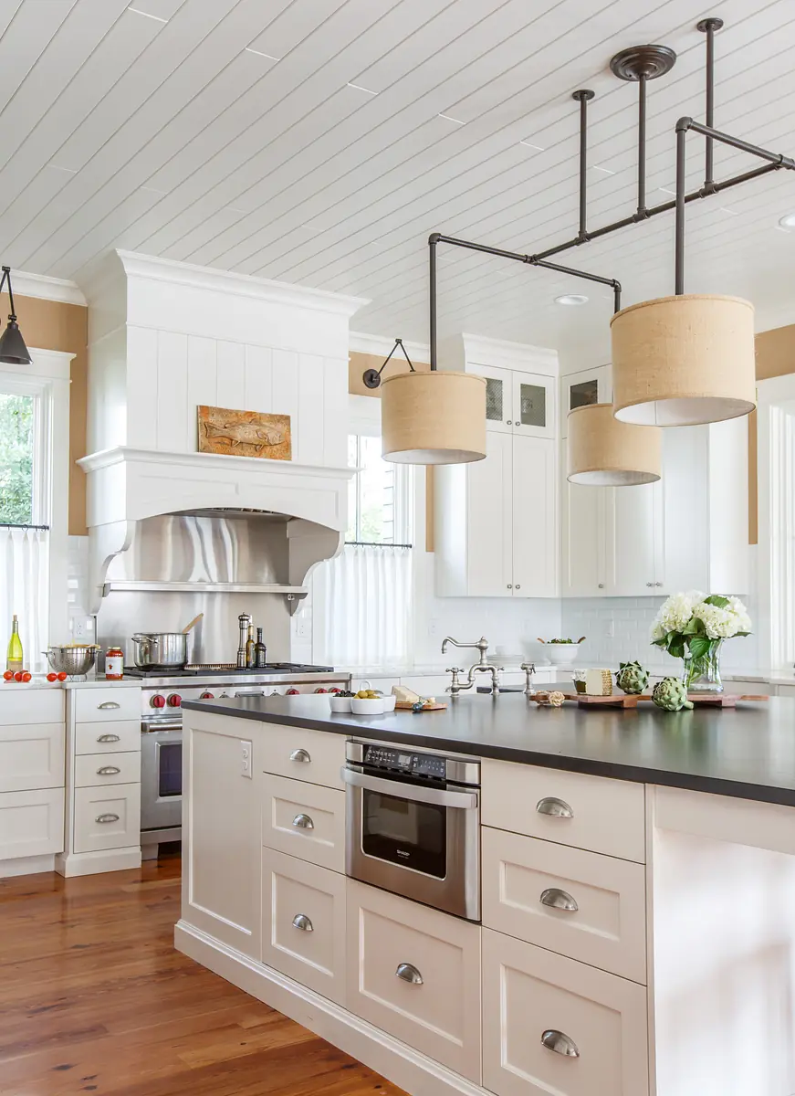 Kitchen with white cabinetry, black countertop island, stainless steel oven, and beige walls with wooden flooring.