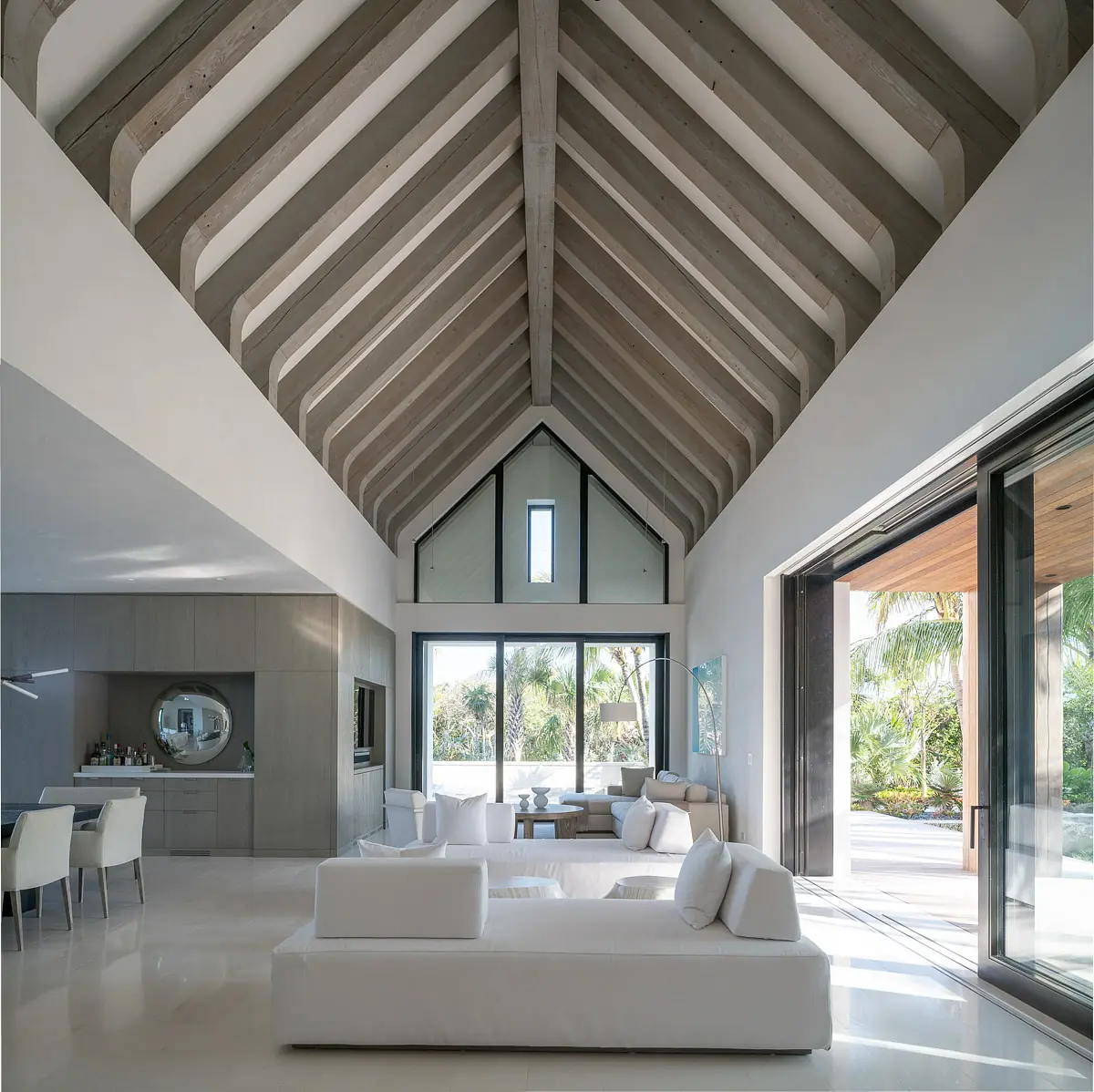 Living room with white sofa, accent chairs, coffee table, large glass doors, and exposed wooden beams.