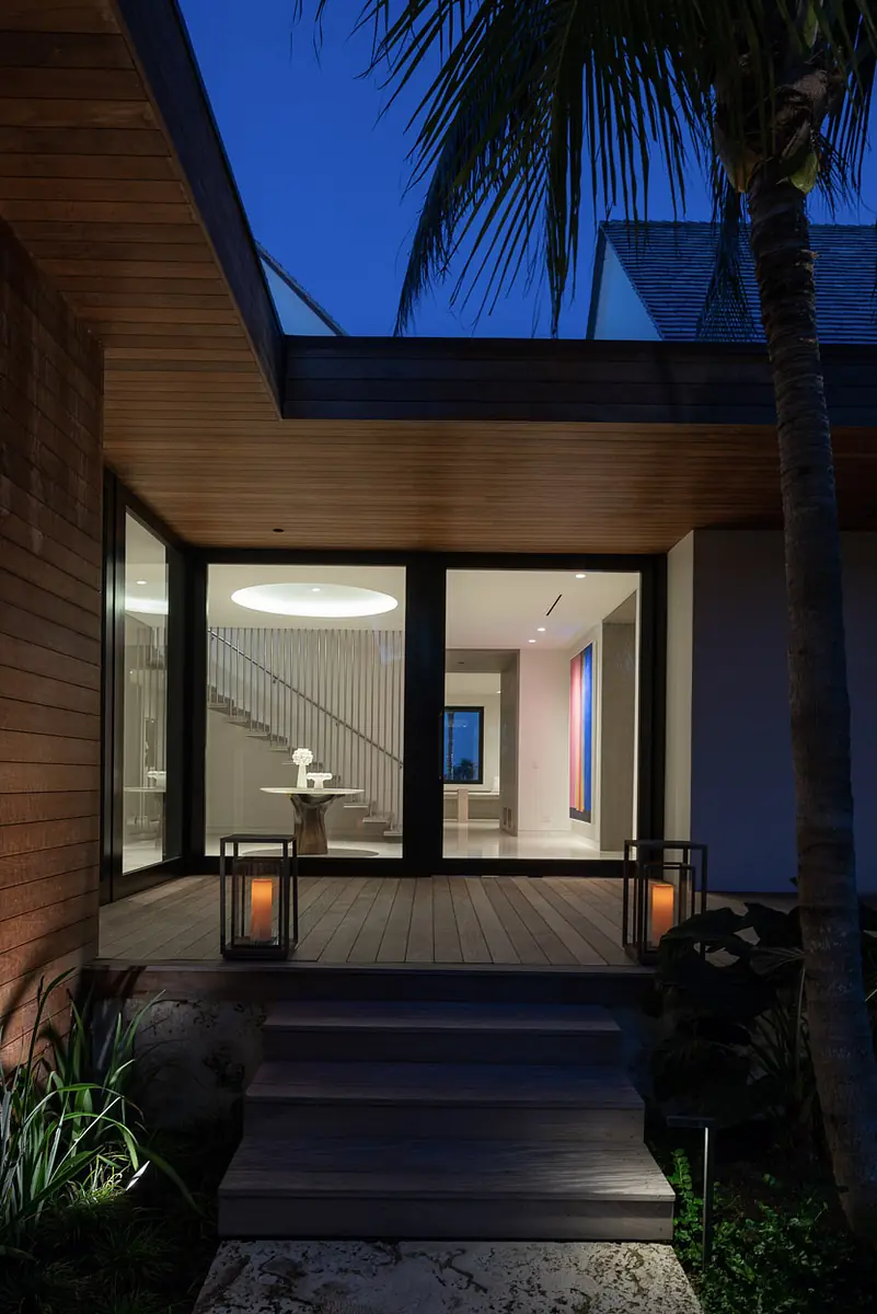 Exterior front view of a house with wooden deck, glass doors, potted plants, and lanterns.
