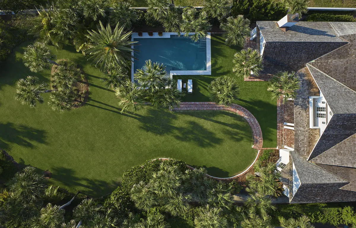 Garden with green lawn, palm trees, swimming pool, lounge chairs, and curved brick pathway