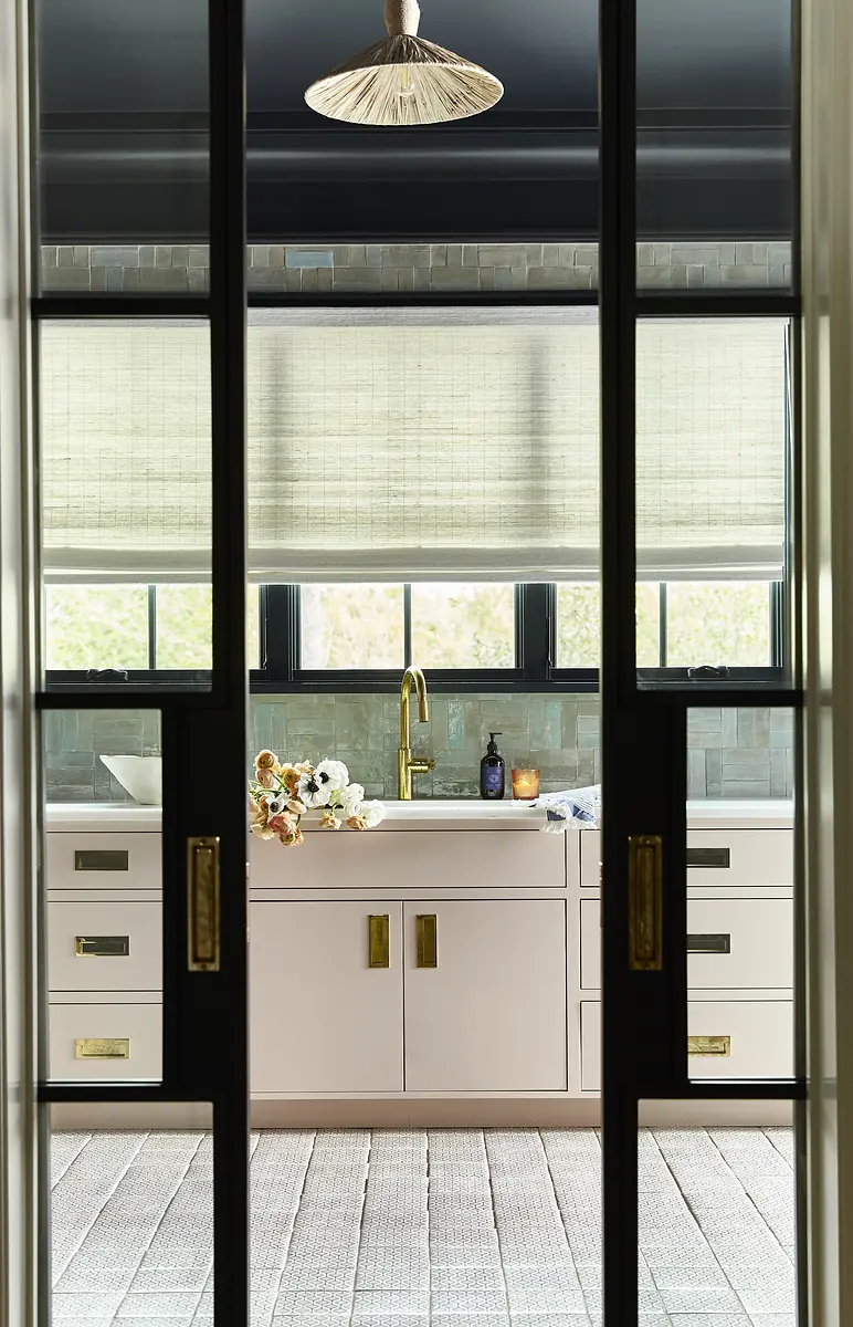 Kitchen with light cabinetry, sink area, flowers, and large window with woven shades.