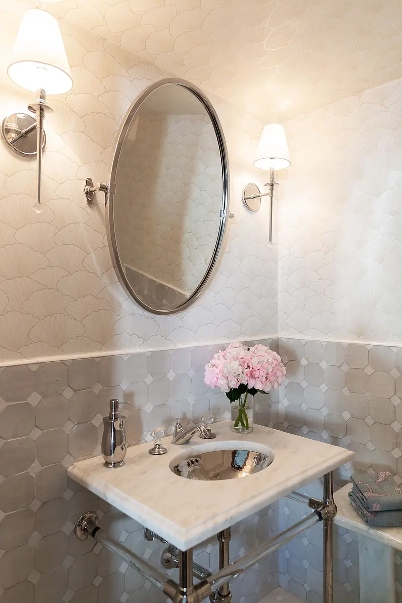 Powder room with marble vanity, circular mirror, wall-mounted sink, and pink flower bouquet.