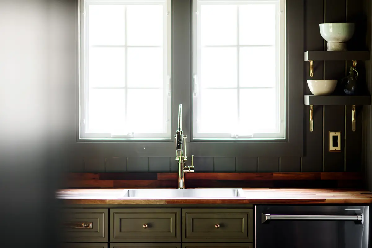 Kitchen with dark cabinetry, wooden countertop, stainless steel sink, and windows for natural light.