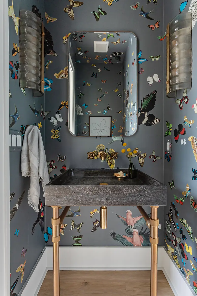 Powder room with butterfly wallpaper, sink, mirror, towel, and flowers on a light wood floor.