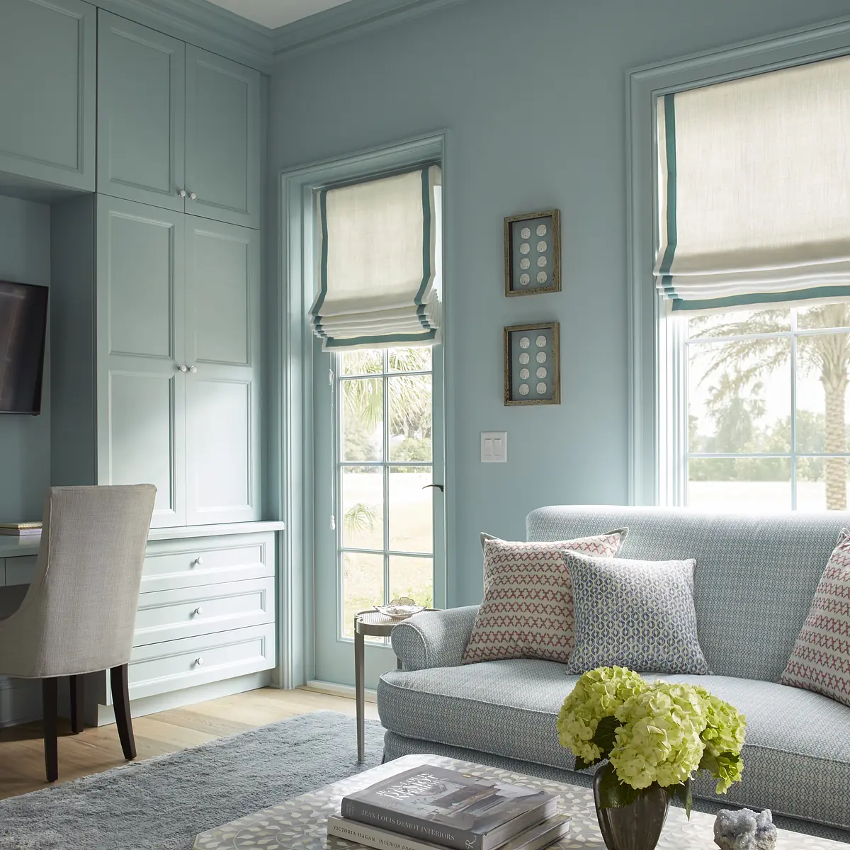 Office with light blue walls, blue sofa, grey rug, built-in cabinetry, and dual windows.