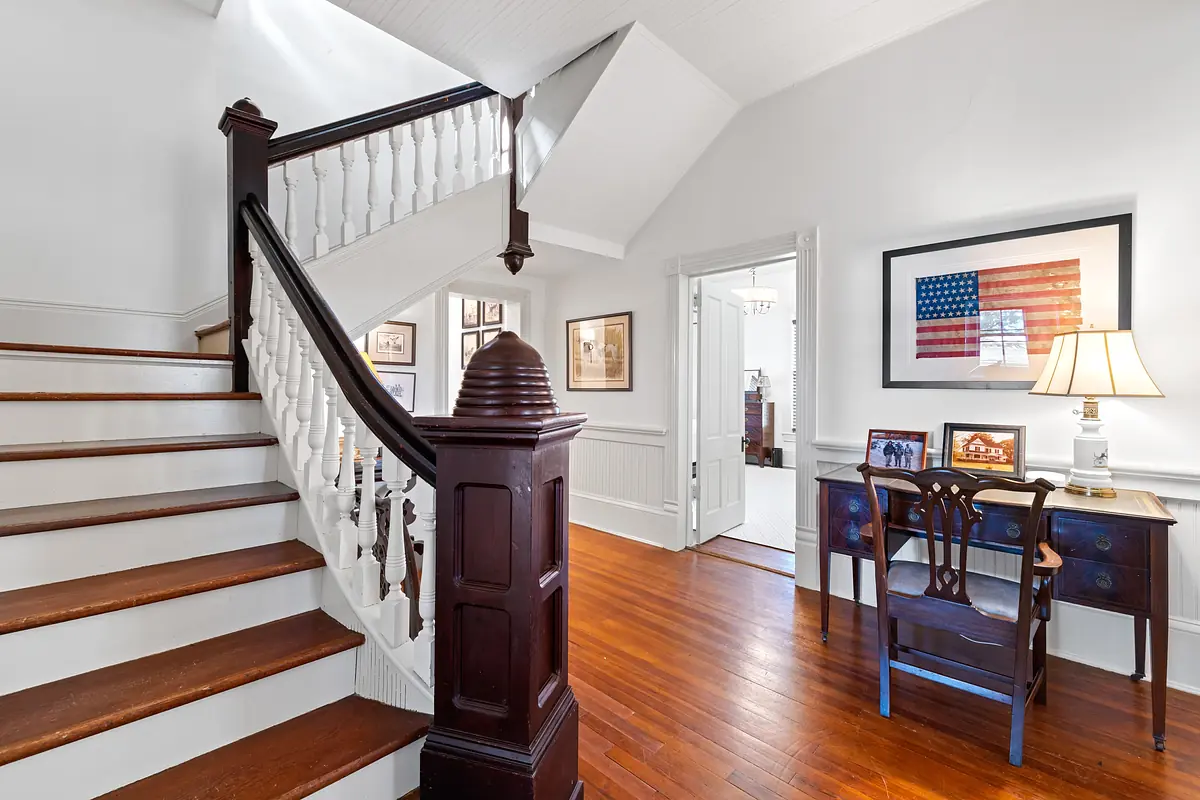 Foyer with wooden staircase, accent table, lamp, framed artwork, and hardwood flooring.