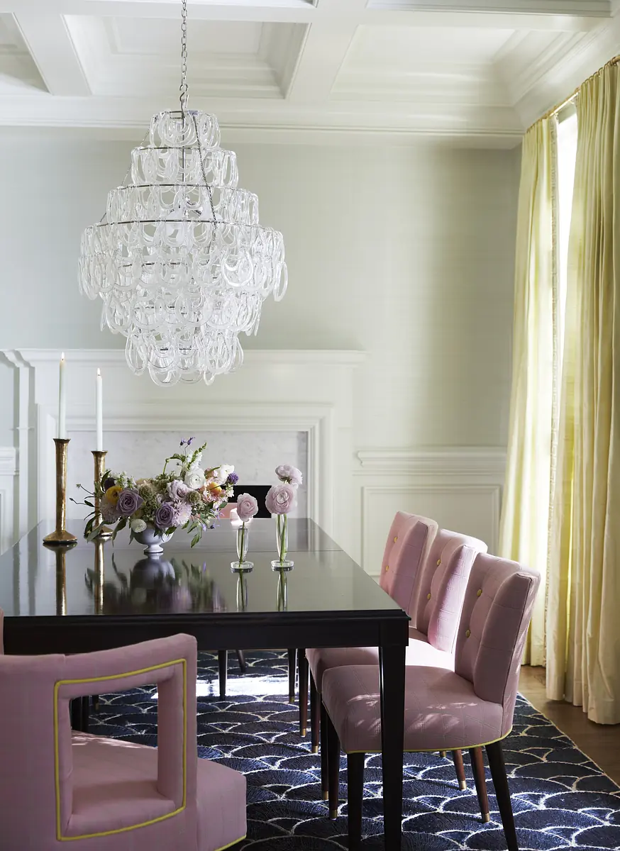 Dining room with black table, pink chairs, floral centerpieces, chandelier, and patterned rug.