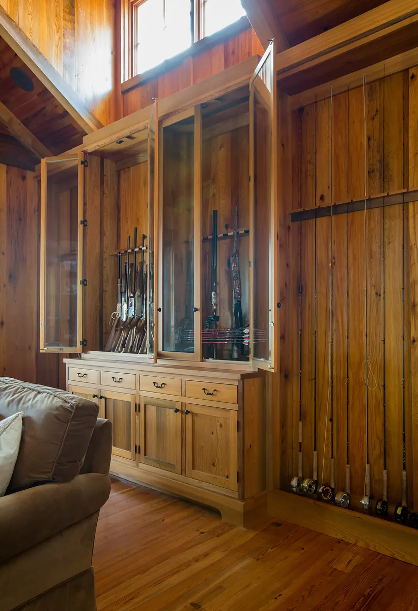 Living room with wooden walls, beige sofa, display cabinet, and mounted fishing poles.