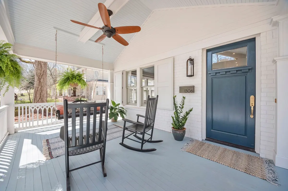 Front porch with rocking chairs, door, potted plant, and hanging planter on a light blue floor.