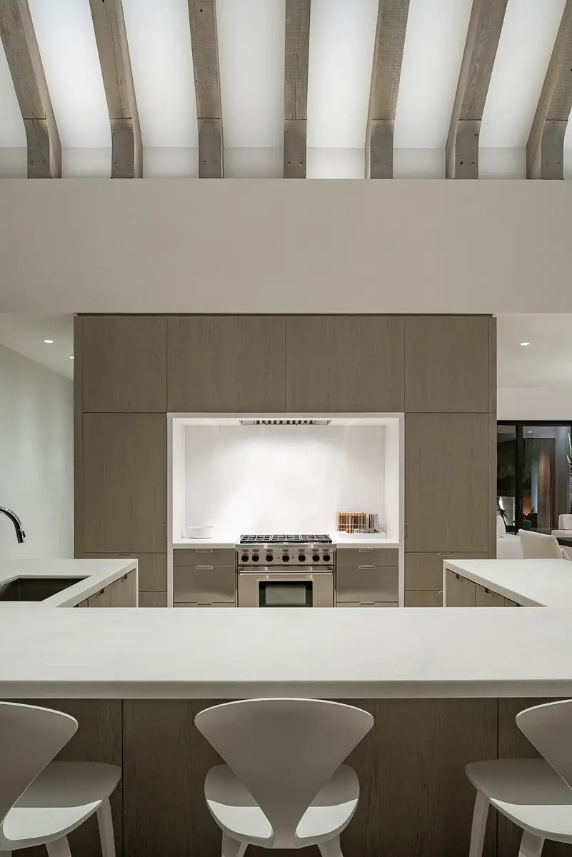 Kitchen with central island, bar stools, wood cabinetry, built-in oven, and exposed beams with natural light.