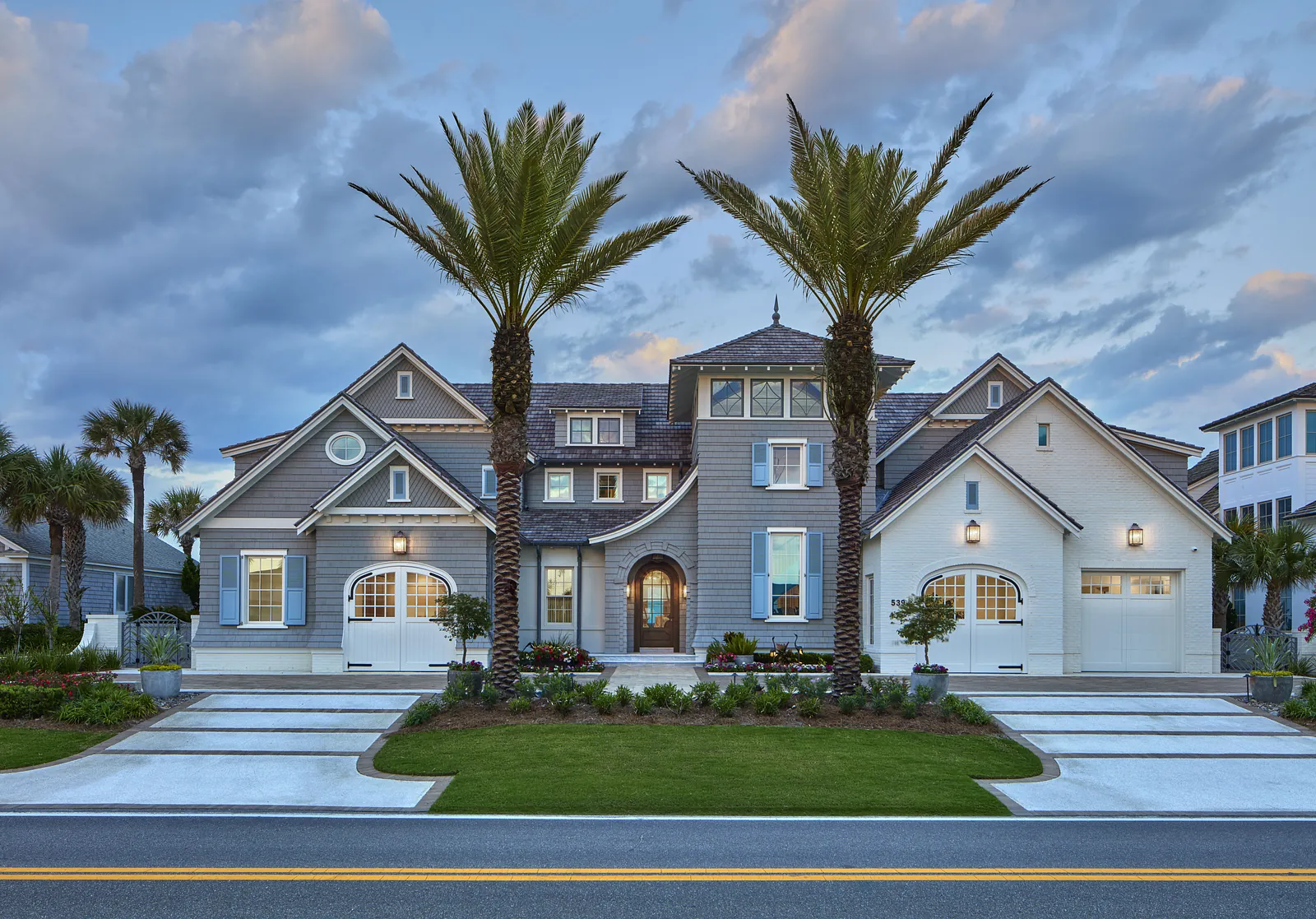 Exterior view of a house with gabled roofs, garage doors, palm trees, and a landscaped yard.