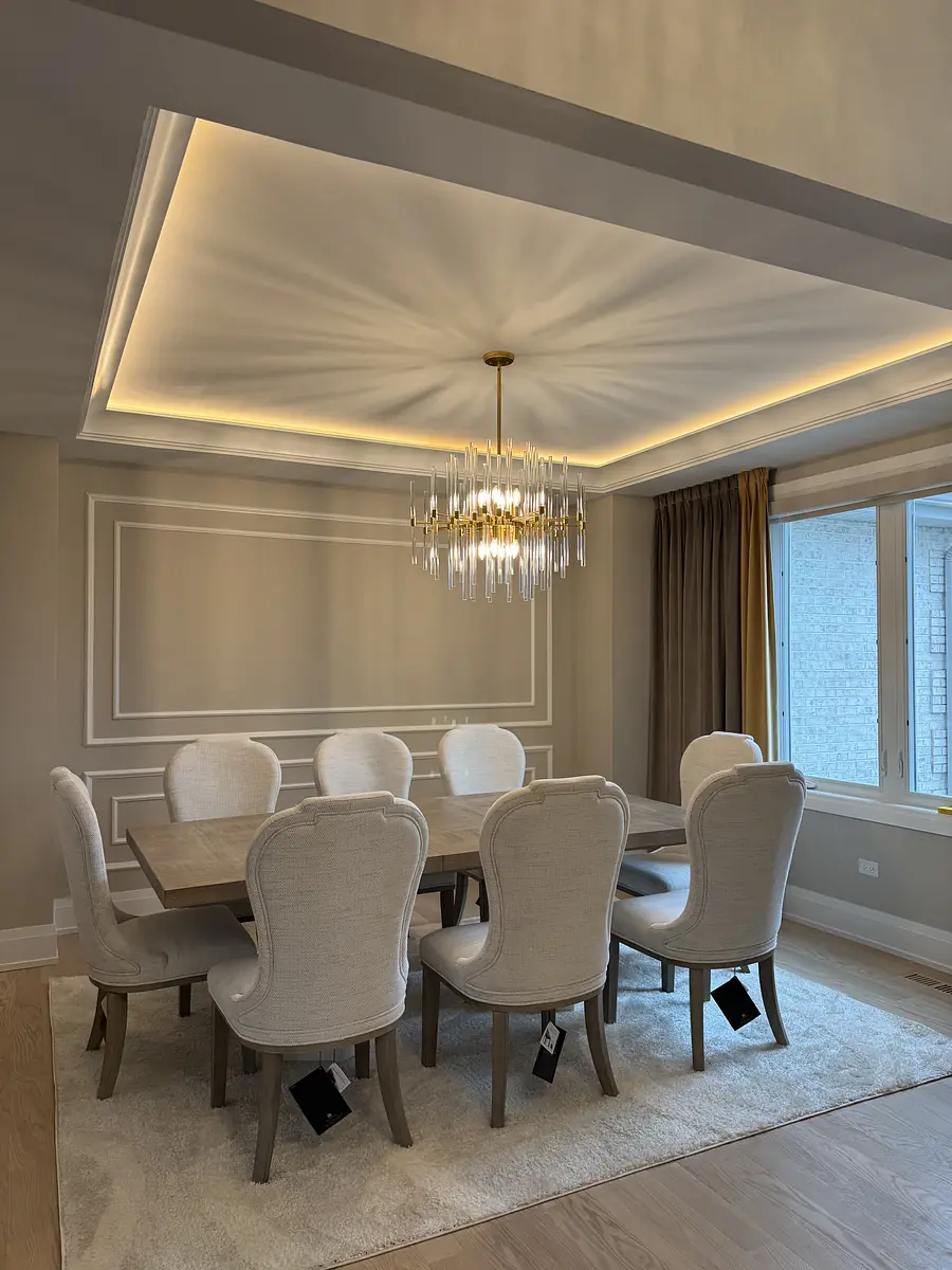 Dining room with wood table, upholstered chairs, crystal chandelier, decorative paneling, and large window.