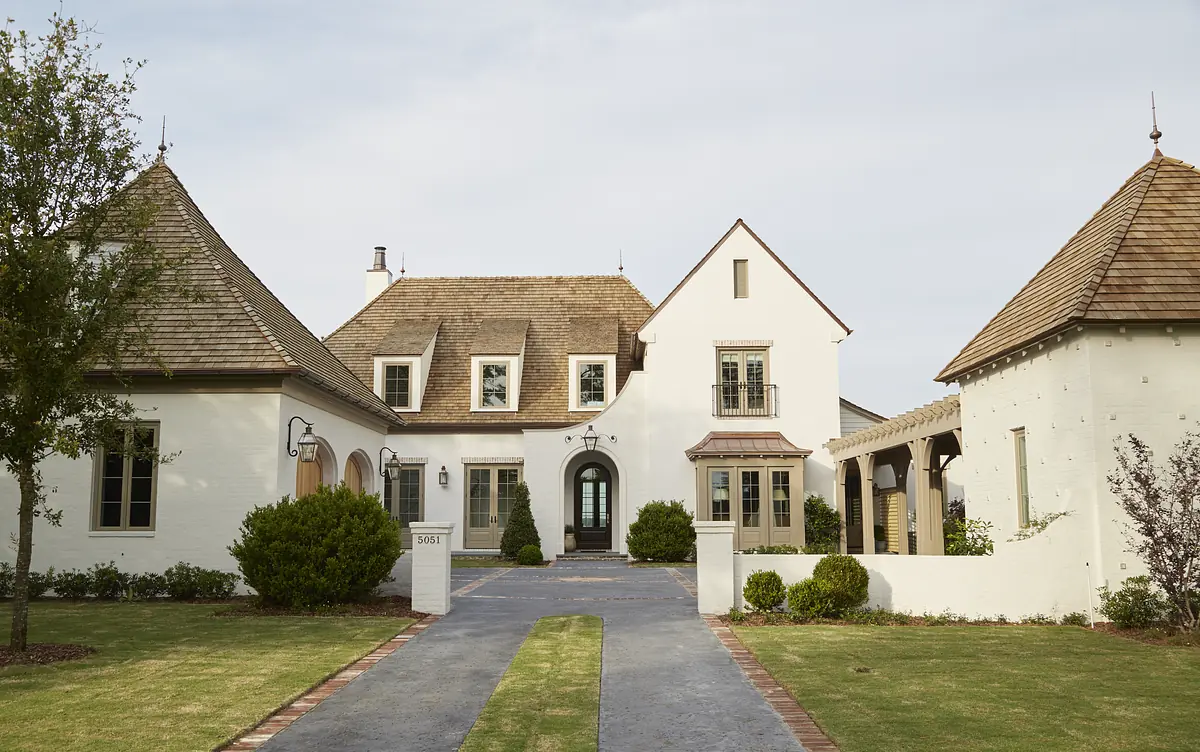 Exterior front view of a house with stucco facade, gabled roofs, stone pathway, and landscaped greenery.