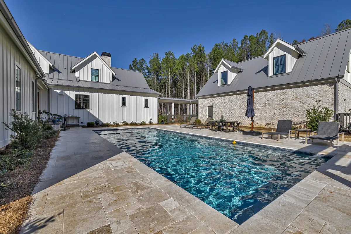 Outdoor space with pool, stone patio, lounge chairs, and surrounding buildings.