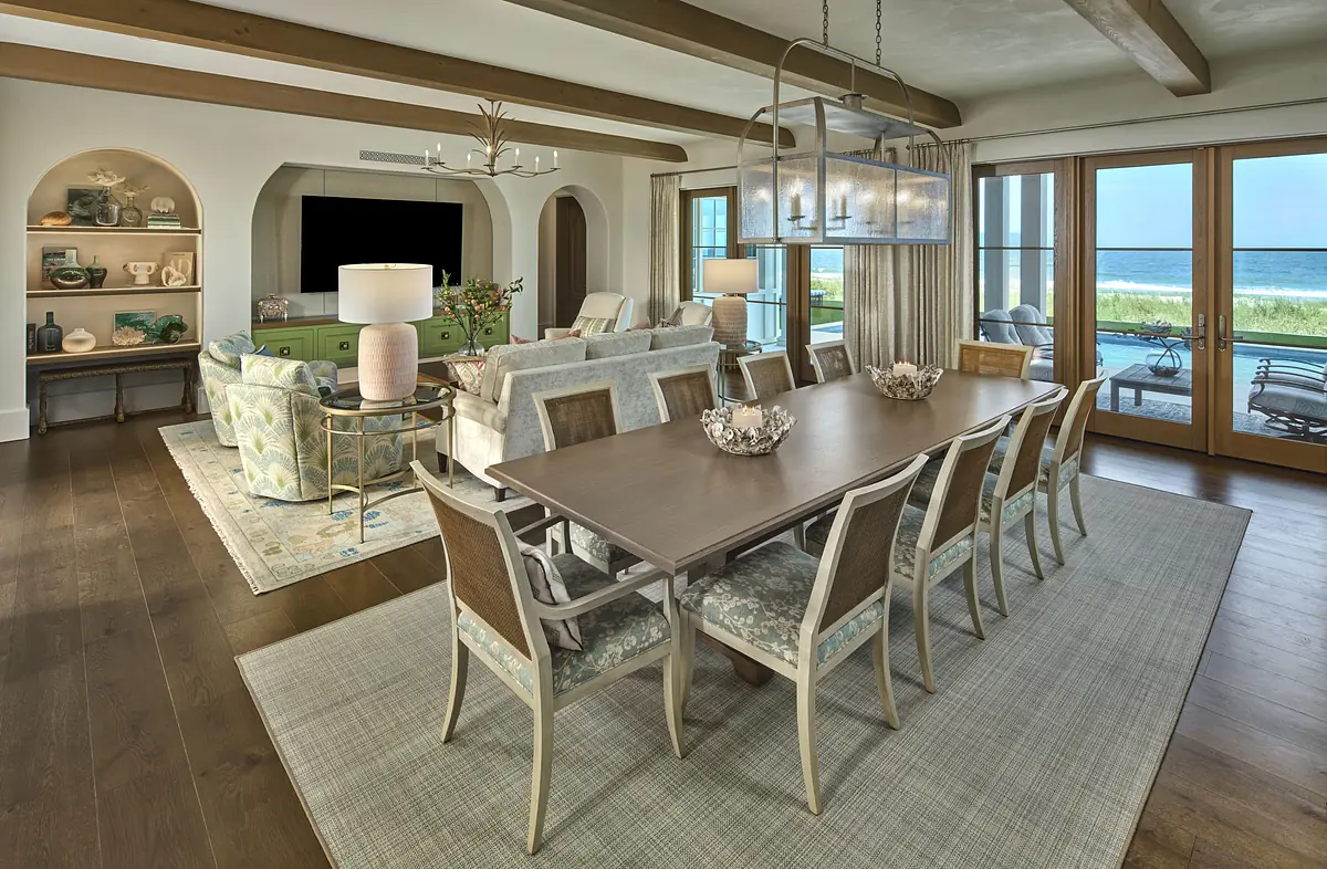 Dining room with wooden table, eight chairs, area rug, sideboard, and large glass doors.