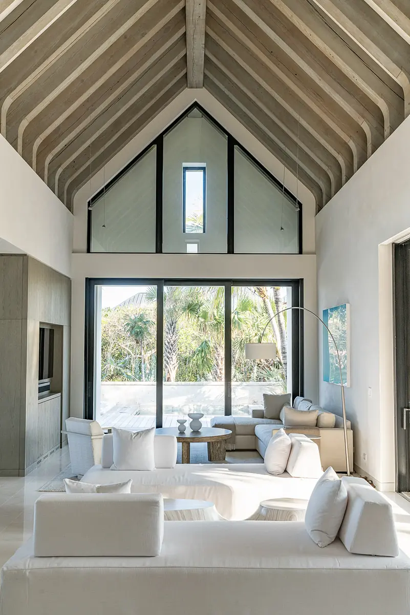 Living room with large sectional sofa, round coffee table, high sloped ceiling, and large glass windows.