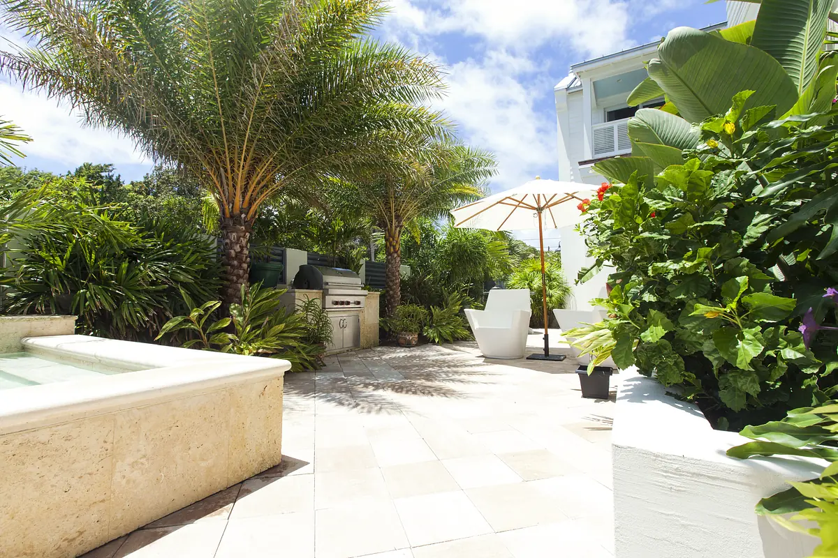 Patio with grill, outdoor chairs, umbrella, hot tub, and surrounding greenery and planters