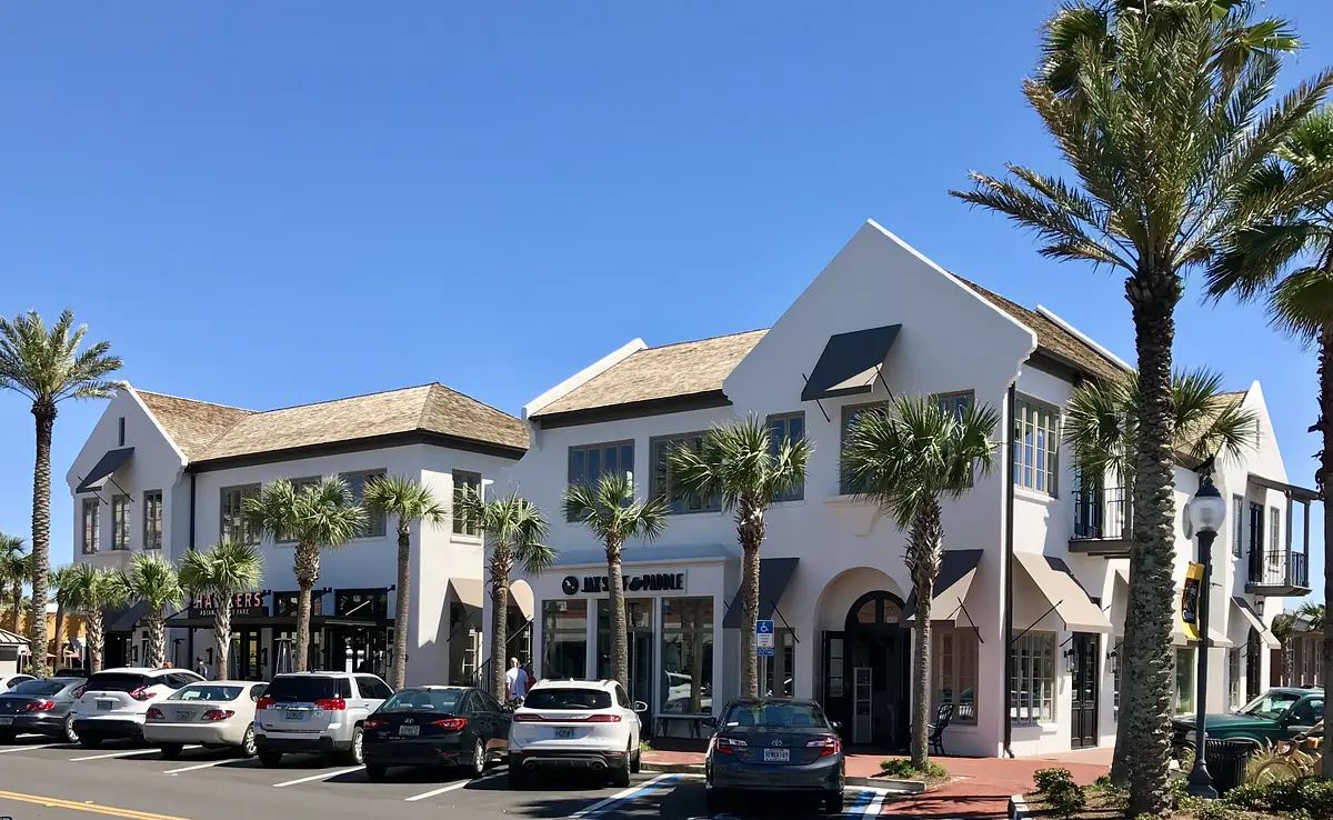 Exterior front of a two-story building with large windows, palm trees, and multiple storefronts.
