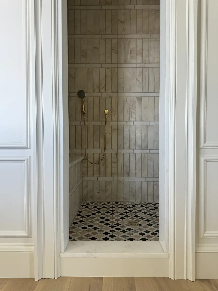 Bathroom with tiled shower area, black and white floor tiles, and gold shower fixtures.