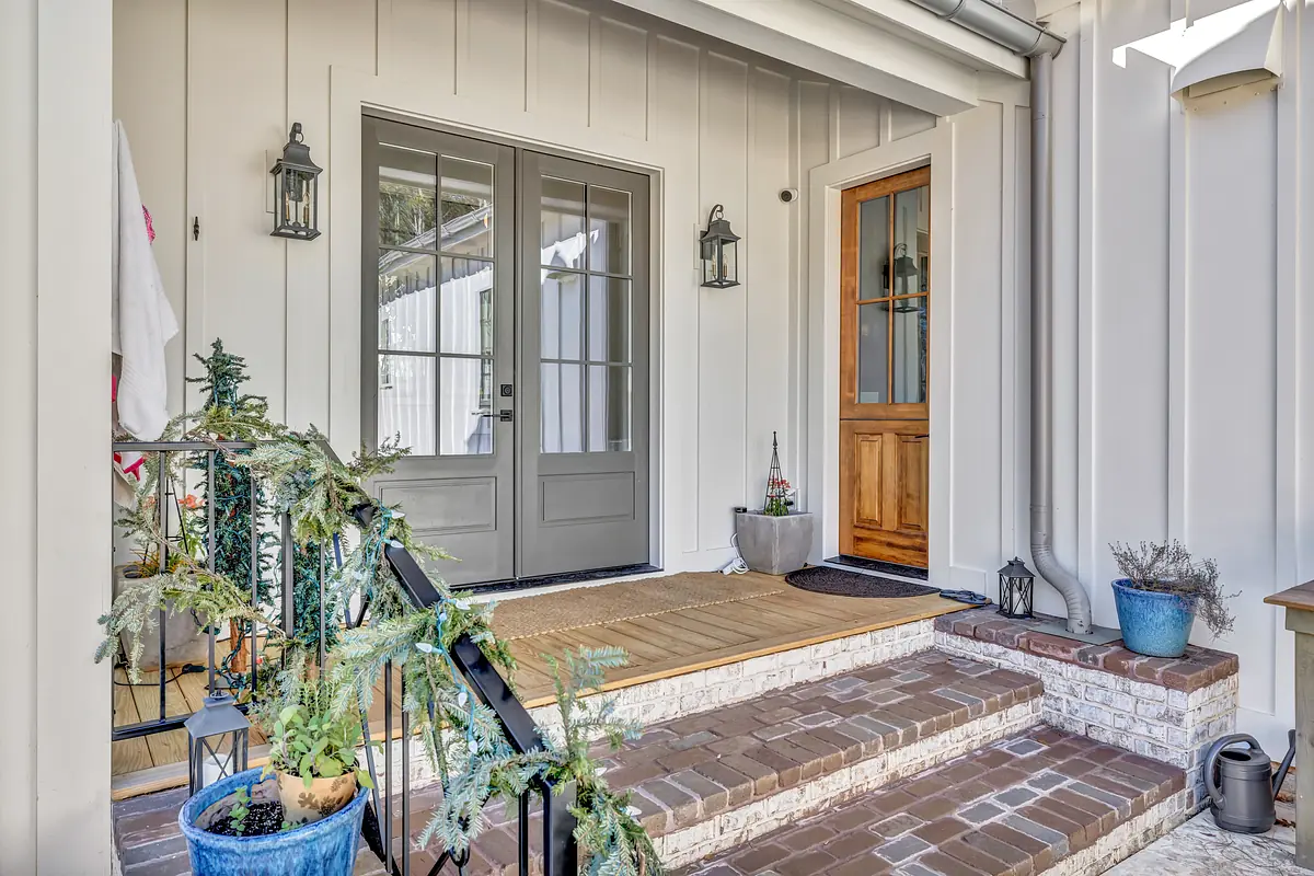 Exterior front entrance with gray double doors, brick pathway, planters, and decorative accents.