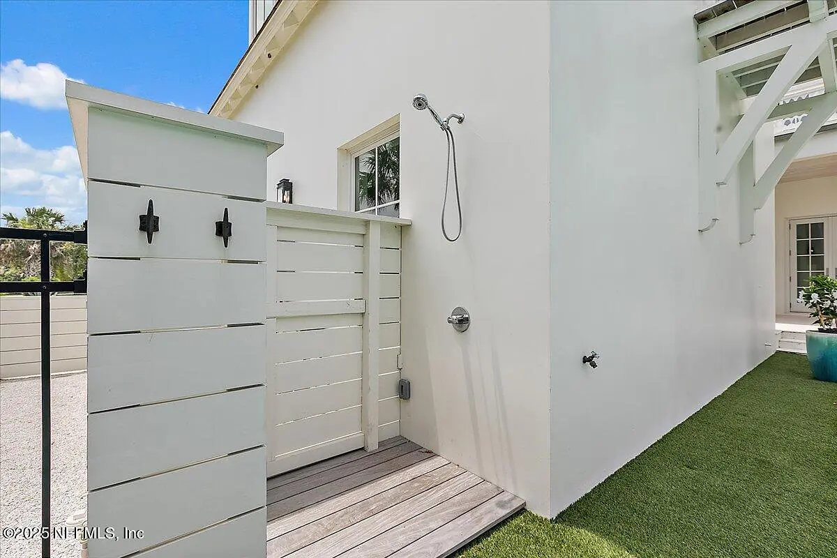 Exterior rear space with wooden outdoor shower, gray decking, privacy wall, and artificial grass.