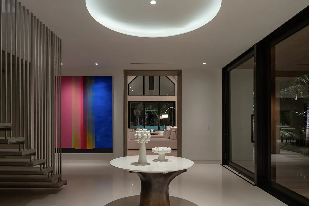 Foyer with round white table, wooden base, vase, artwork, and large glass sliding doors.