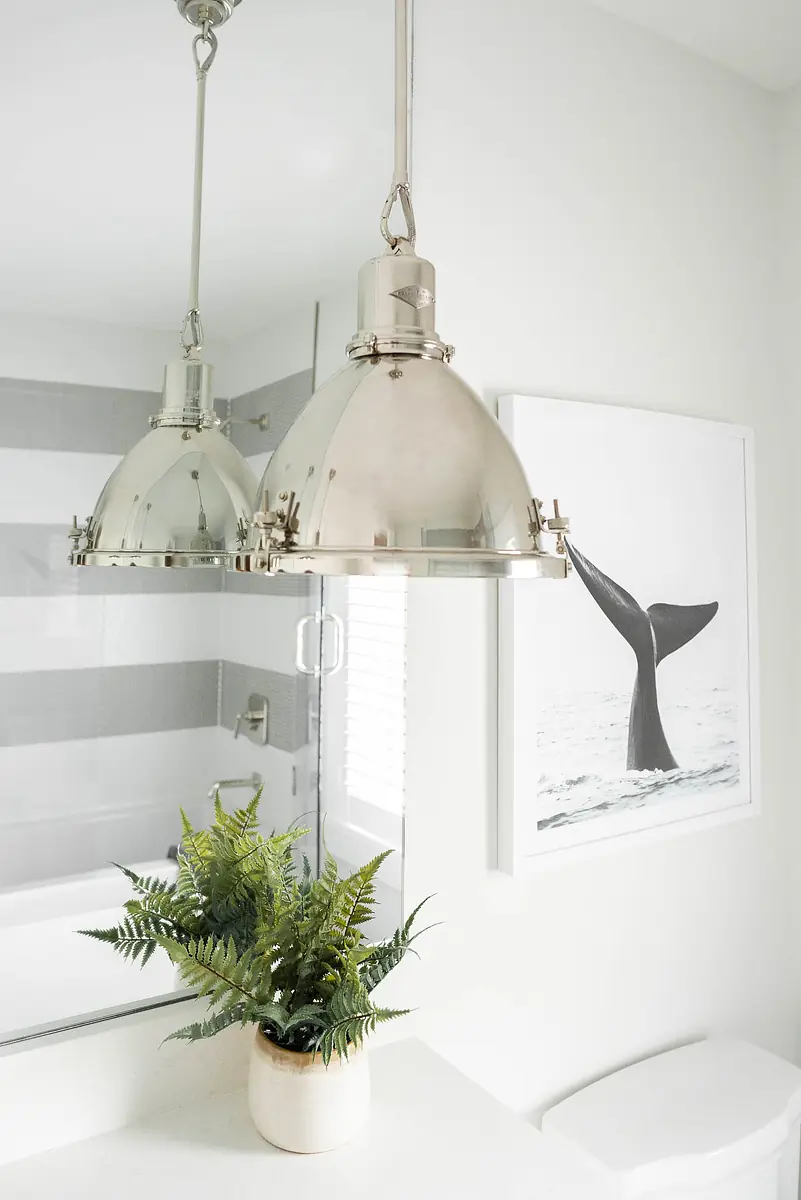 Bathroom with pendant light, mirror, whale art, and potted fern on countertop with striped walls.