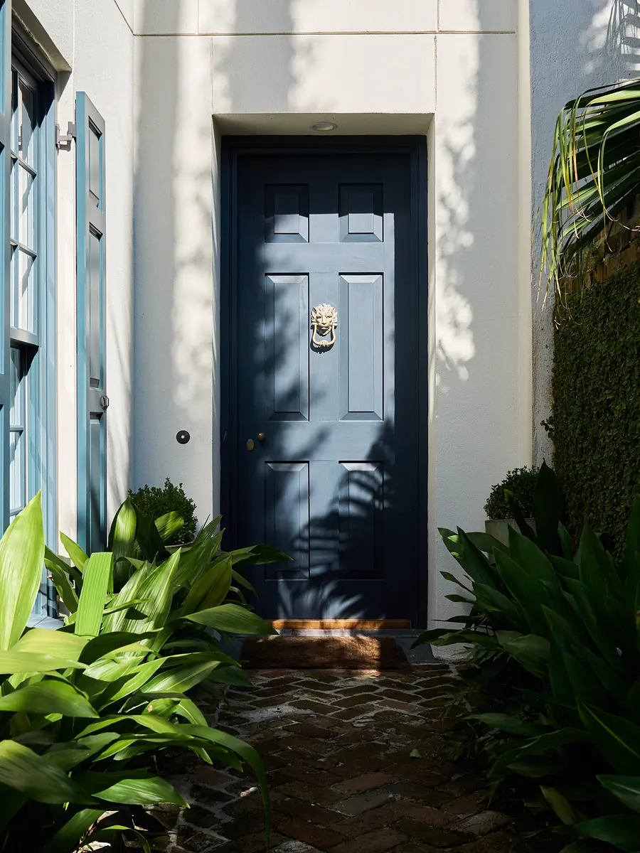 Exterior entry with blue door, lion head knocker, greenery, and brick pathway.